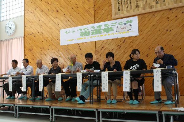 市長や審査委員の男女が舞台の上に並んで座り試食をしている写真
